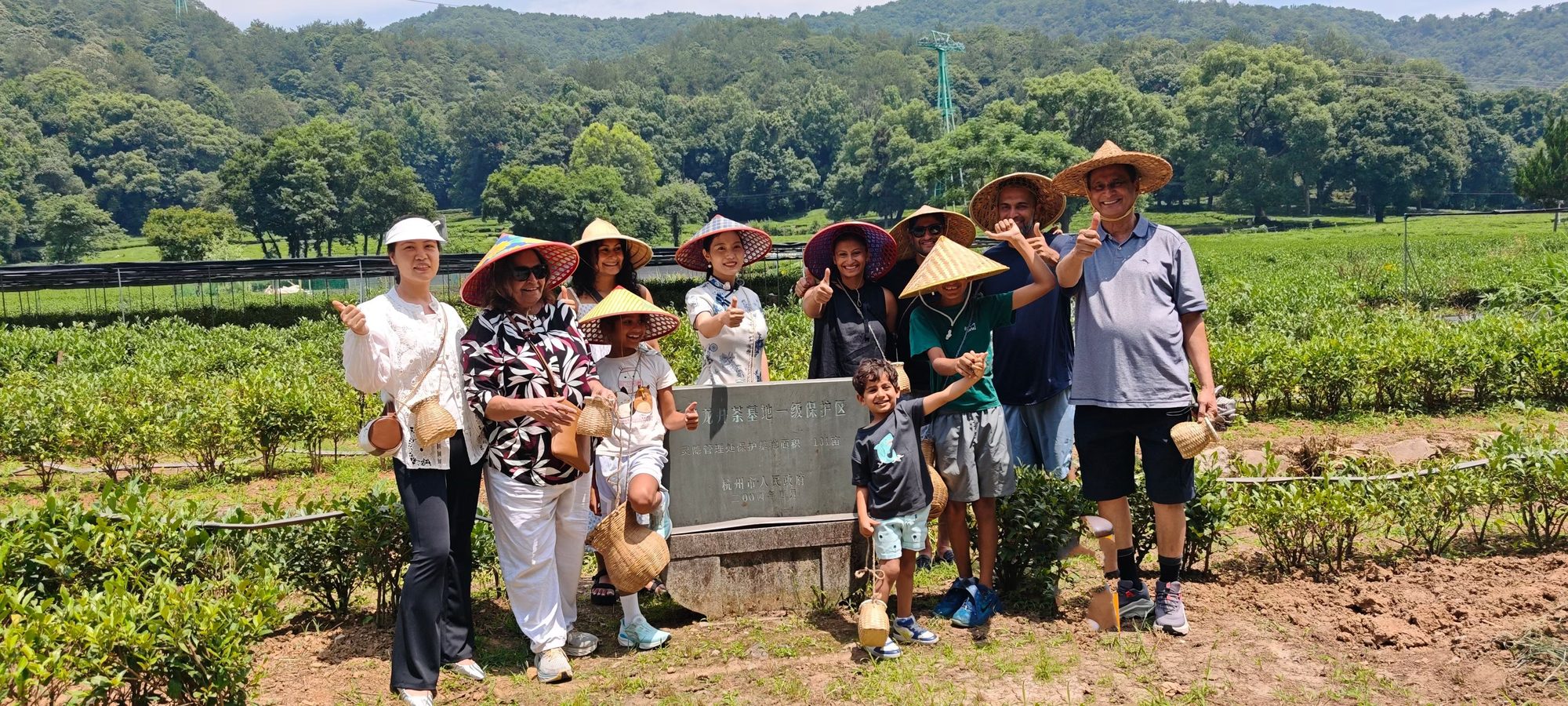 International guests photographed before the stone marker of the West Lake Longjing Grade-1 Protected Base — the family tea garden of Mulan