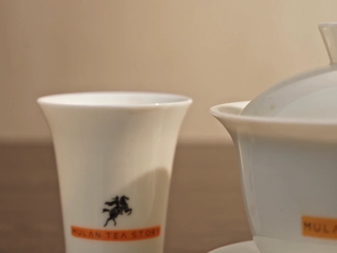Tea table close-up: white porcelain gaiwan, glass fairness cup and tasting cups on dark stone